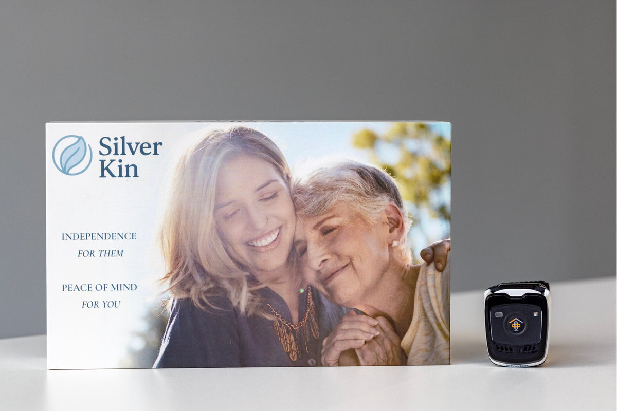 Silver Kin product packaging box shown on a white surface against a gray background, with a small black smartwatch placed to the right. The box features the Silver Kin logo and a photo of a smiling woman and older woman.