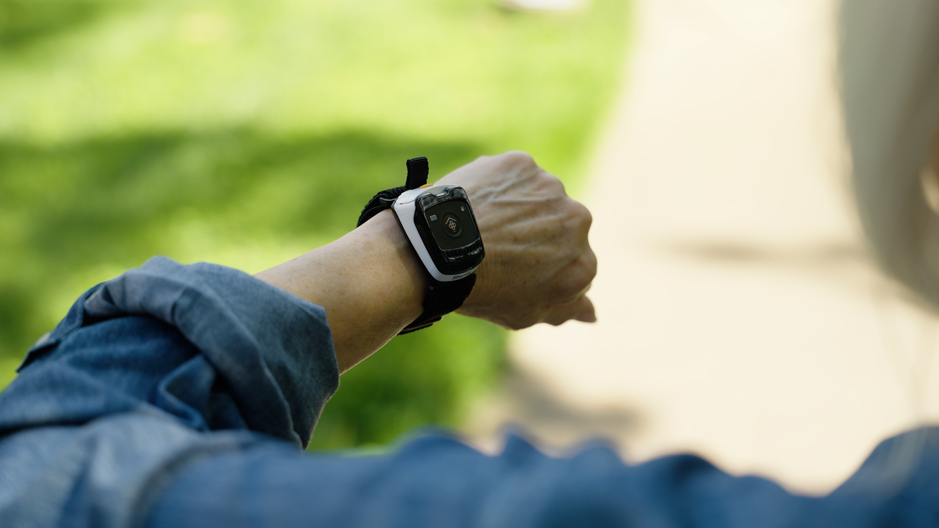 A close-up of a person's wrist wearing a SilverKin Tempo outdoors, with a blurred green lawn and light-colored path in the background.