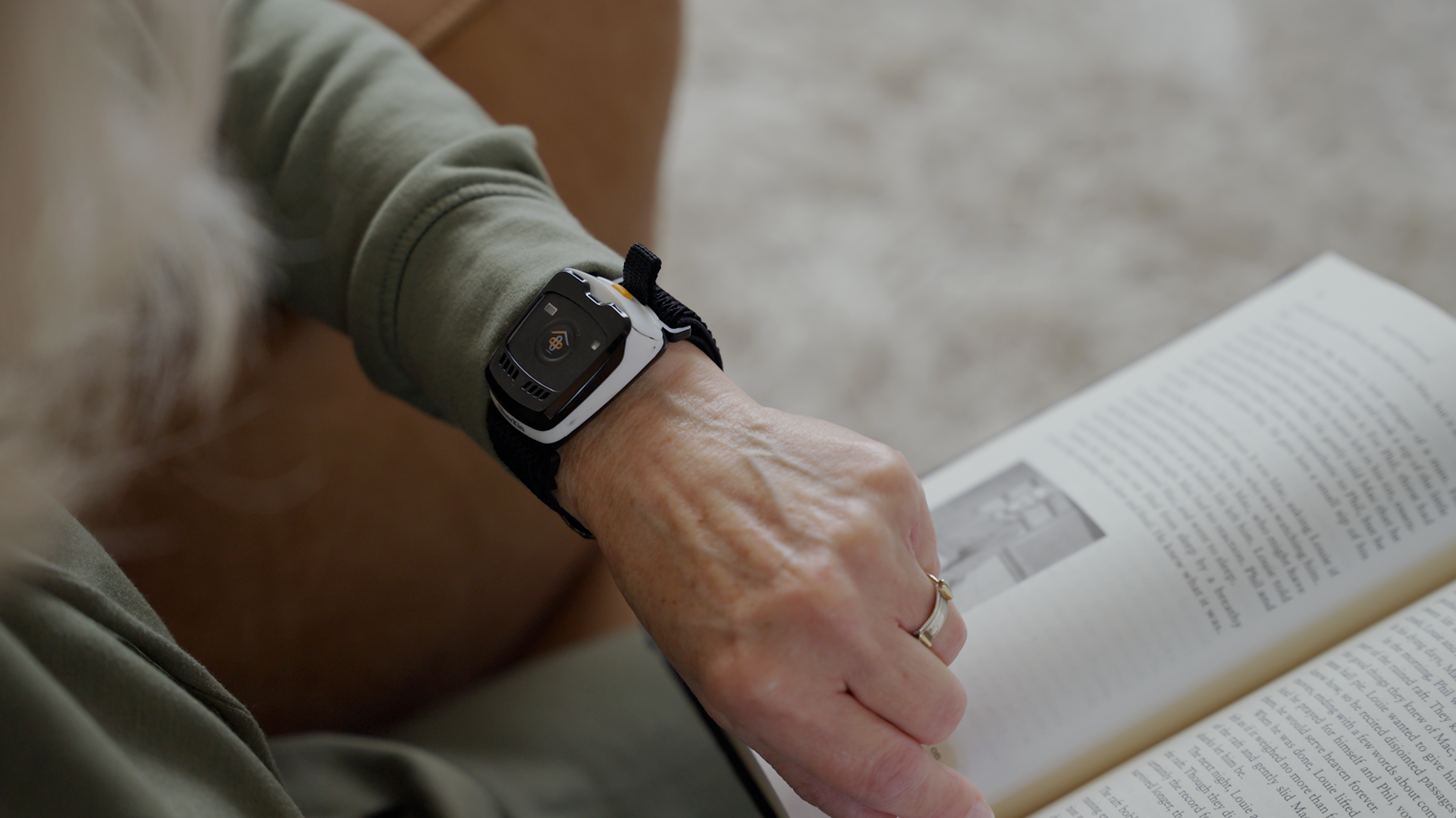 A close-up of a person's hand resting on an open book while wearing a SilverKin Tempo with a black band and a white rectangular case.