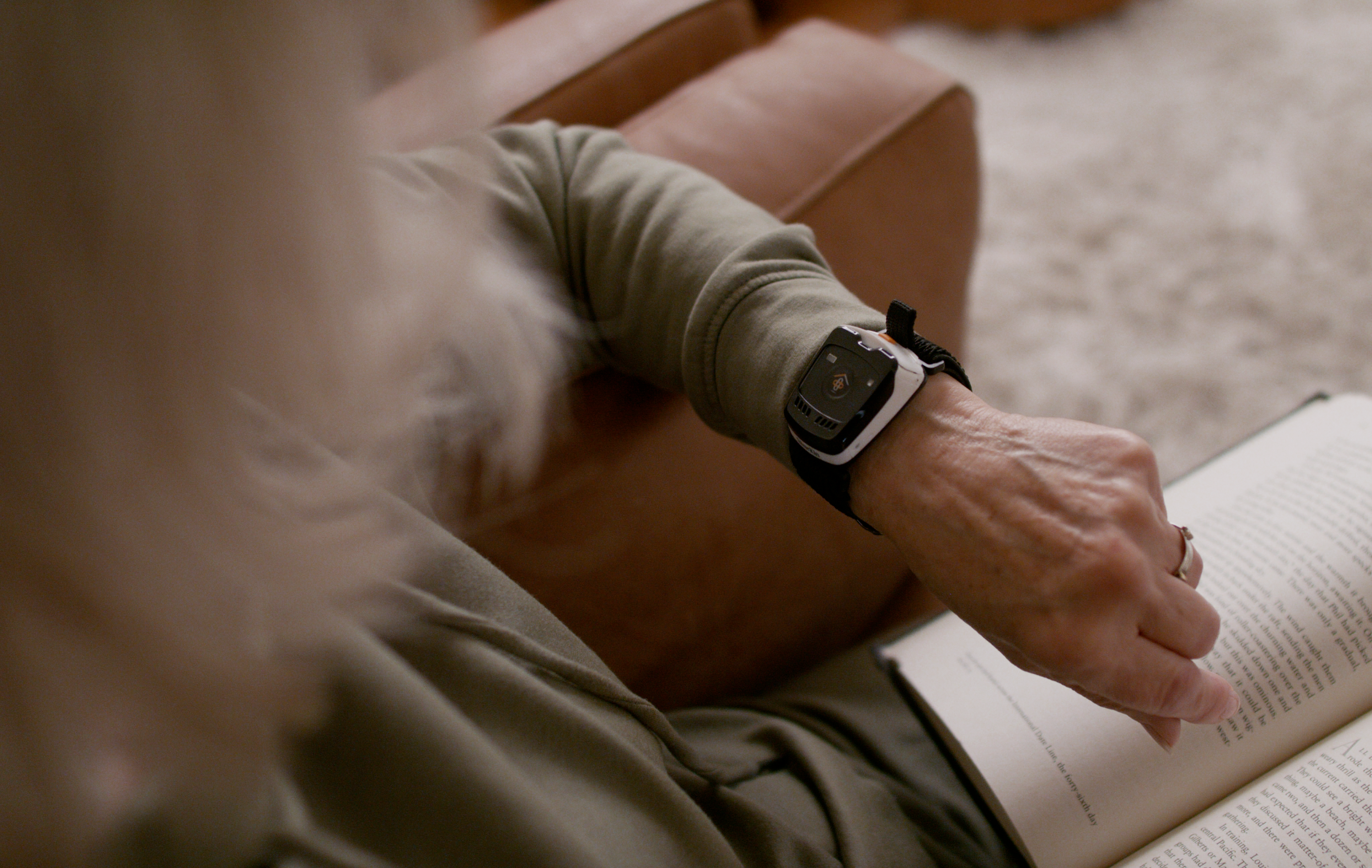 A close-up lifestyle shot of a person sitting in a brown leather armchair, wearing a SilverKin Tempo with a black band on their wrist while holding an open book.